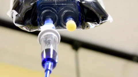 Close-up of an IV drip chamber with a clear fluid, highlighting the drop formation at the tip of the chamber, indicative of IV fluid administration.