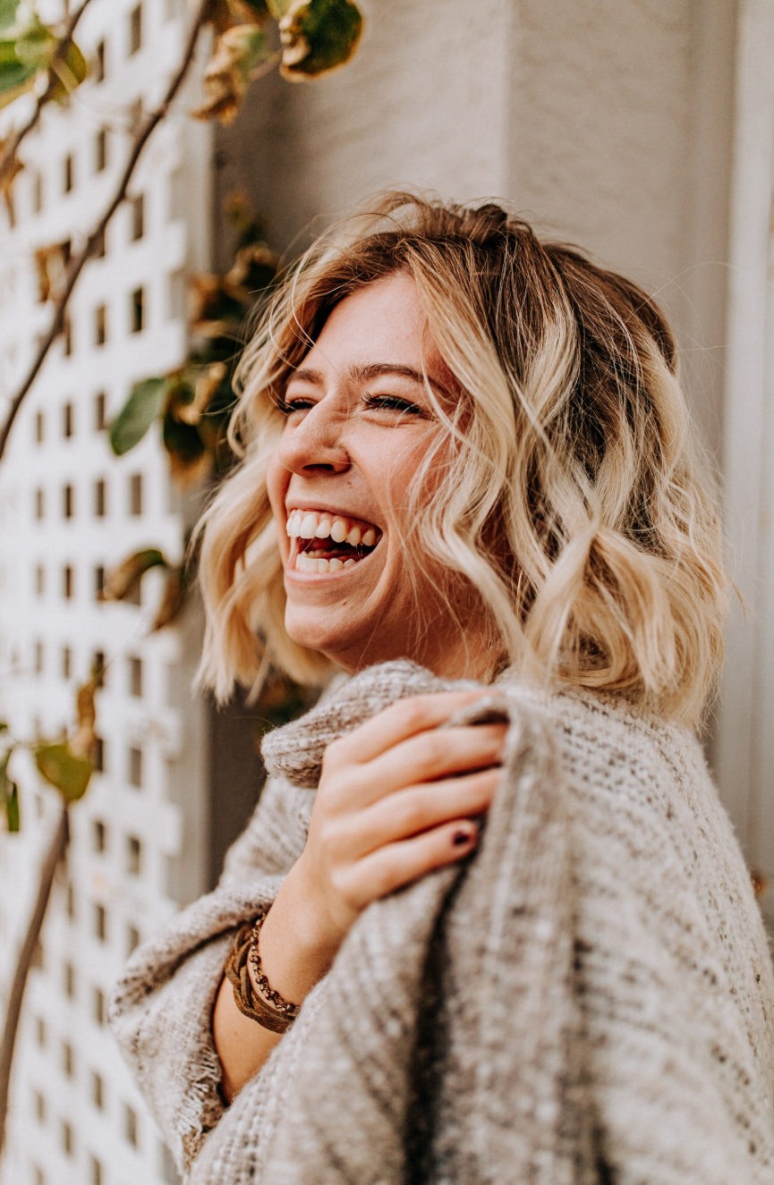 Joyful woman laughing outdoors, wrapped in a cozy sweater.