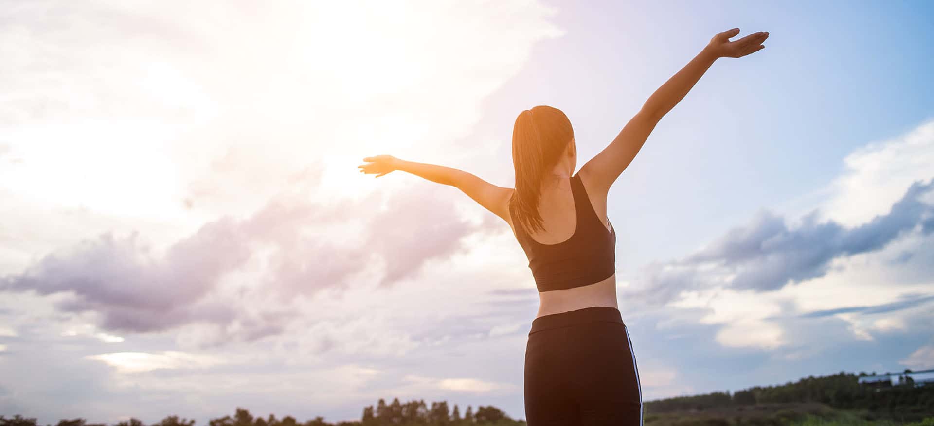 Woman with arms raised celebrating freedom at sunset