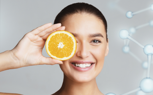 A joyful woman holding a slice of orange over her eye, smiling brightly