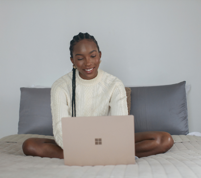 Smiling woman on a bed with a laptop, relaxed and comfortable.