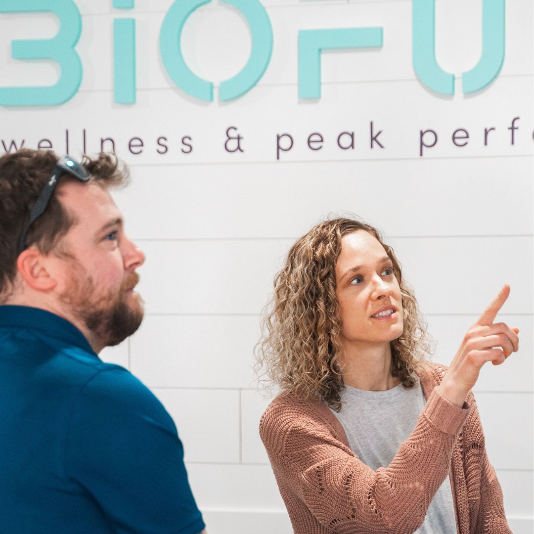 Two people in conversation in front of a Biofuse wellness center sign.