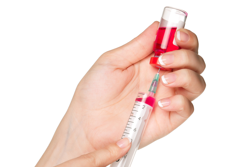 Hand holding a syringe and a red vaccine vial