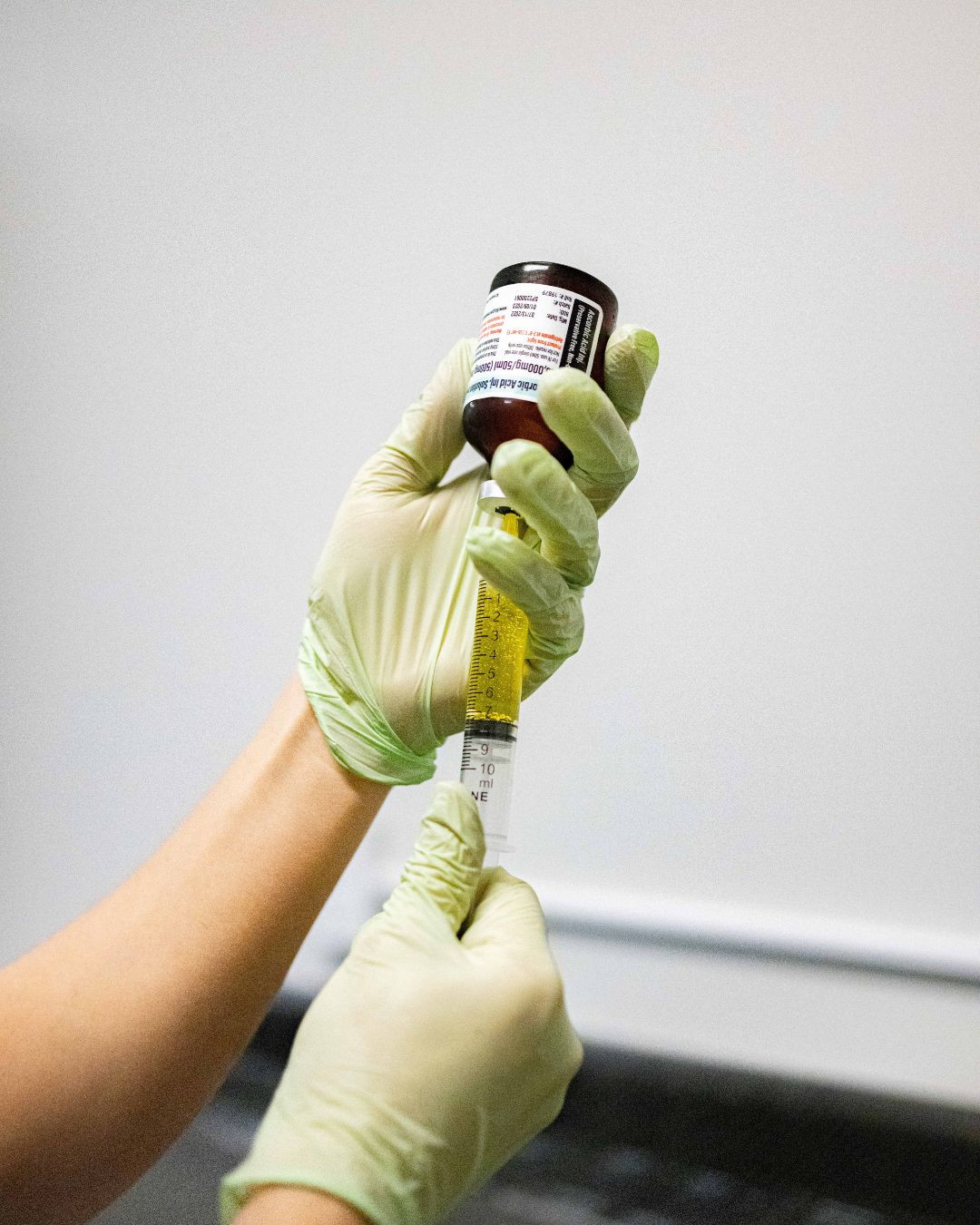 Gloved hand drawing vitamin solution into syringe from a vial.