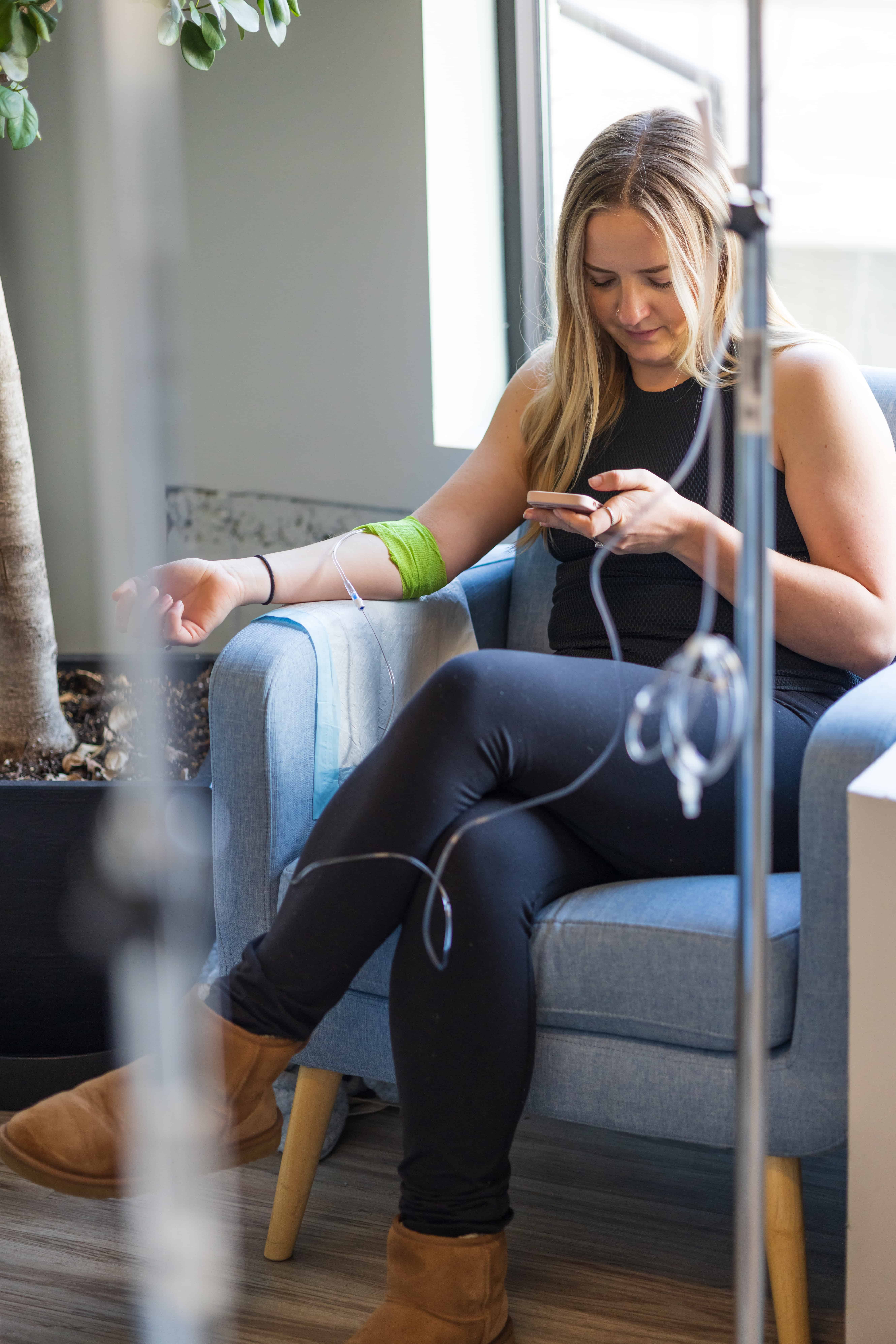 Woman using smartphone while seated during IV therapy session -Biofuse